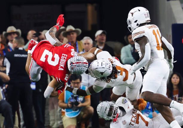 ARLINGTON, TEXAS - JANUARY 10: Emeka Egbuka #2 of the Ohio State Buckeyes leaps over Jaylon Guilbeau #3 of the Texas Longhorns and Jahdae Barron #7 of the Texas Longhorns during the game during the Goodyear Cotton Bowl at AT&amp;T Stadium on January 10, 2025 in Arlington, Texas. (Photo by CFP/Getty Images)